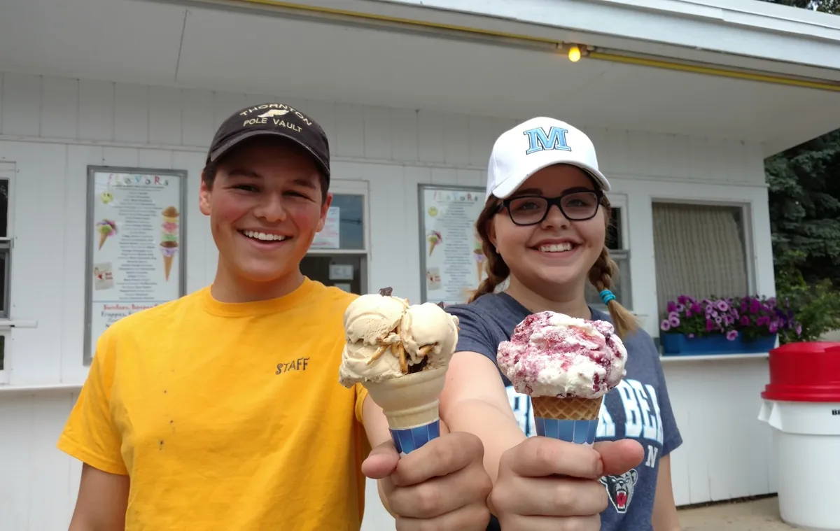 Two Garside's staff in front of the stand, smiling, each holding out an ice cream cone.