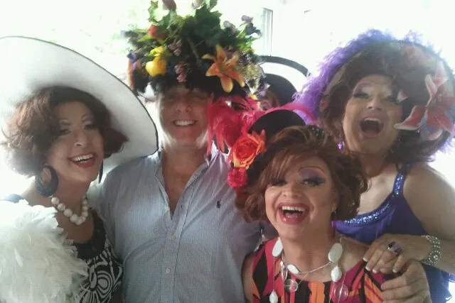 Eric laughing with three drag performers in towering wigs and flowered hats.