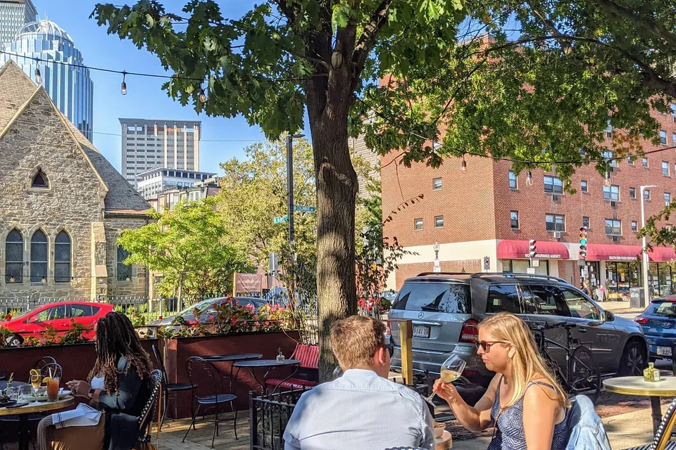 The terrace of a South End bistro under a tree, the Prudential tower behind.