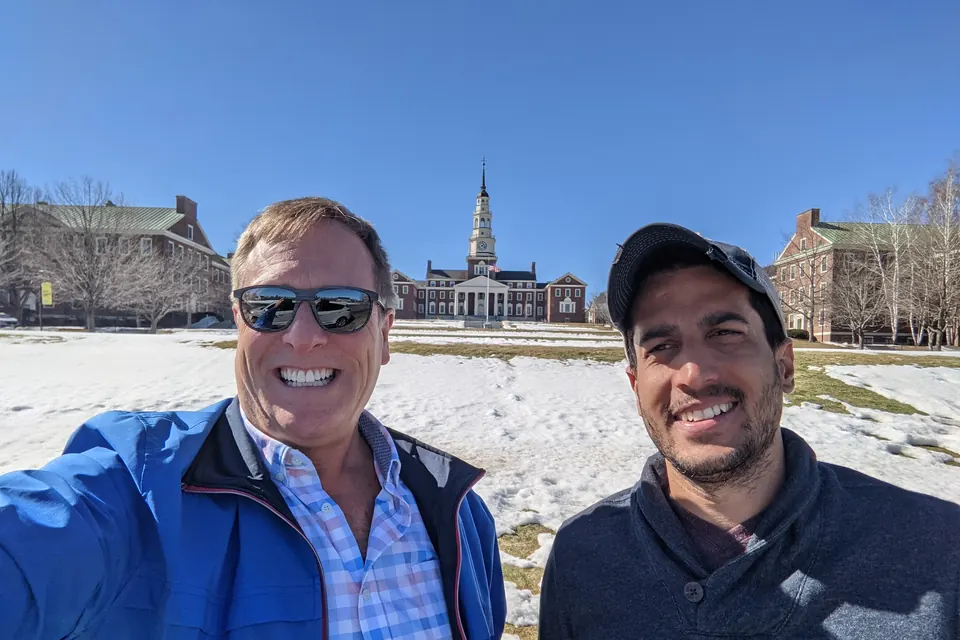 Eric and a friend in a snowy selfie on the Colby College campus, Miller Library's spire behind them.