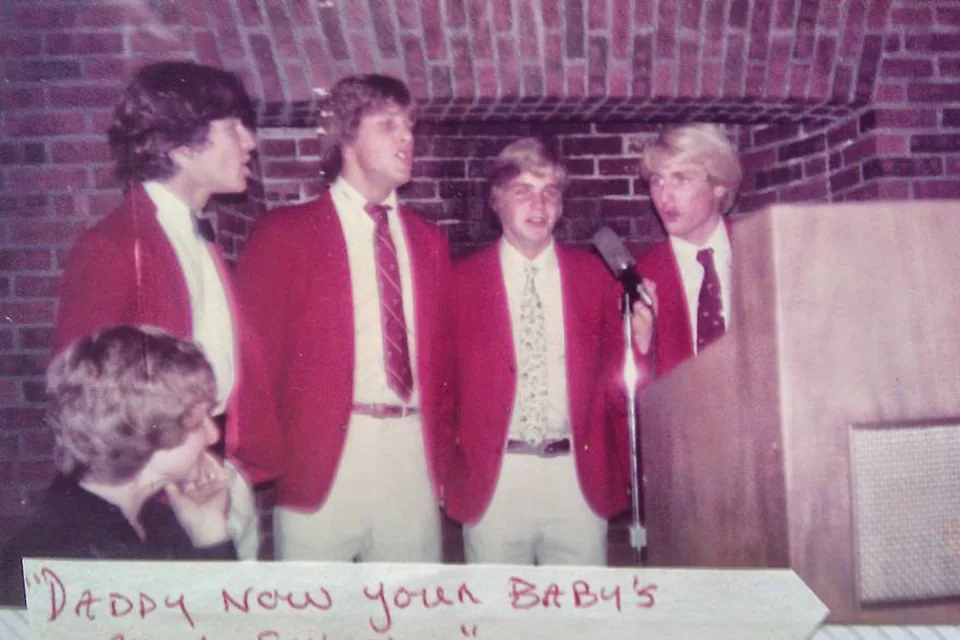 Four students in red blazers singing at a microphone as a barbershop quartet at Exeter.