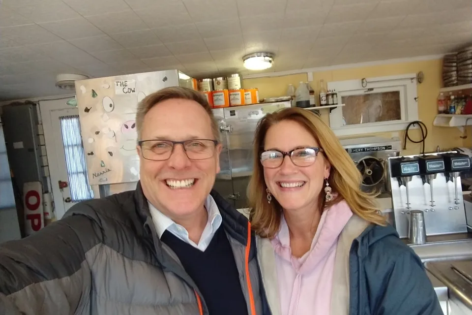 A selfie of Eric with a longtime friend, neighbor and former Garside's employee, both smiling, inside Garside's, with the walk-in freezer and the milkshake mixers behind them.