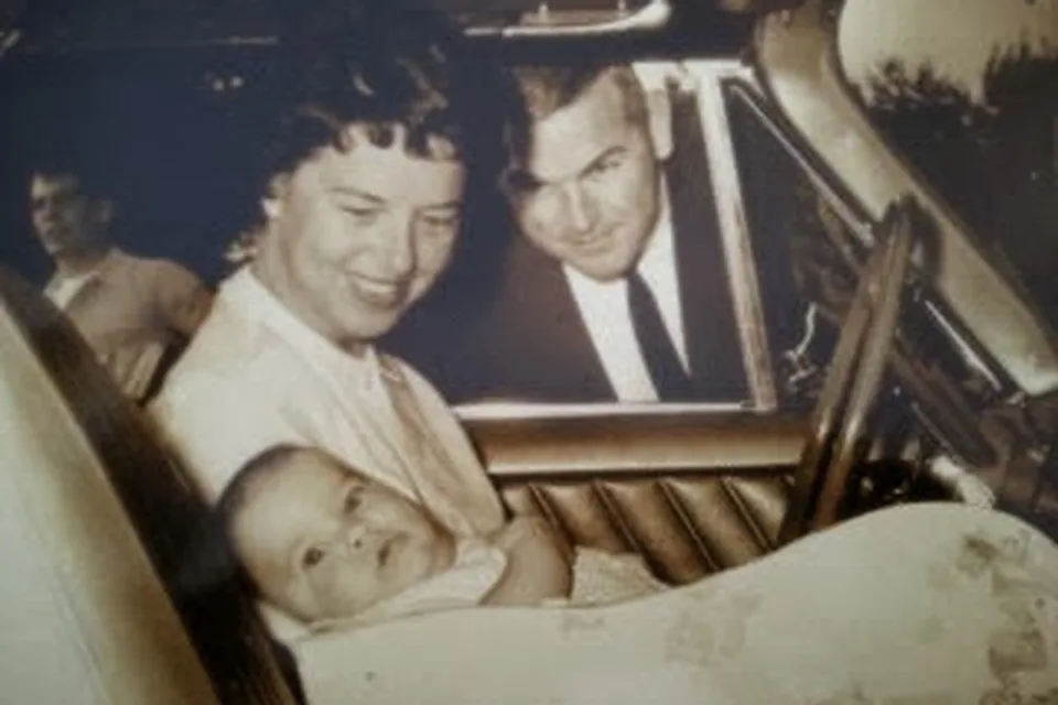 A small old photo of Eric as a baby with his parents in a car.