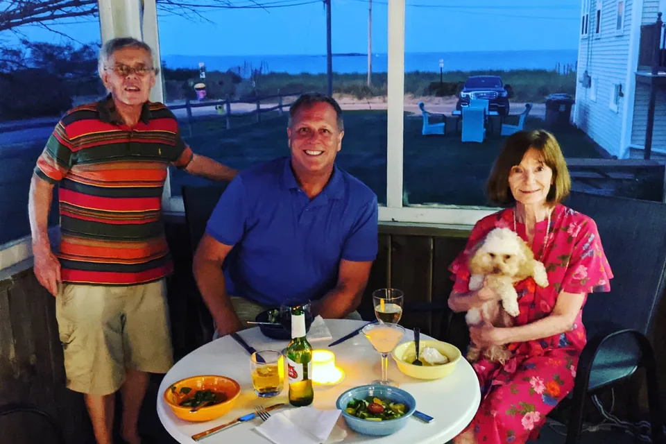 Dinner on a screened porch at dusk in Maine, the beach road and the sea behind.