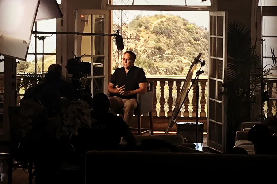 Eric seated for an interview on a film set, lights and camera around him.