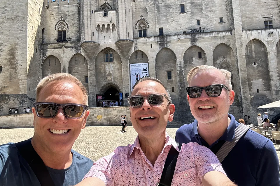 Eric and two friends in sunglasses, grinning, in the square before the Palais des Papes in Avignon.